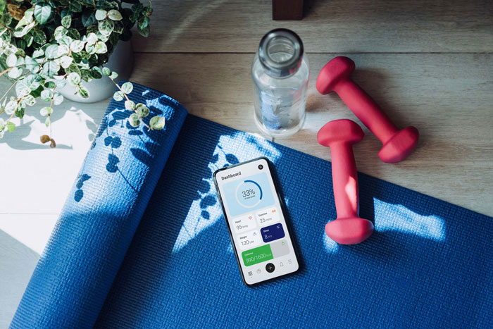 En blå träningmatta med rosa hantlar, en vattenflaska och en mobil som visar en träningsapp.